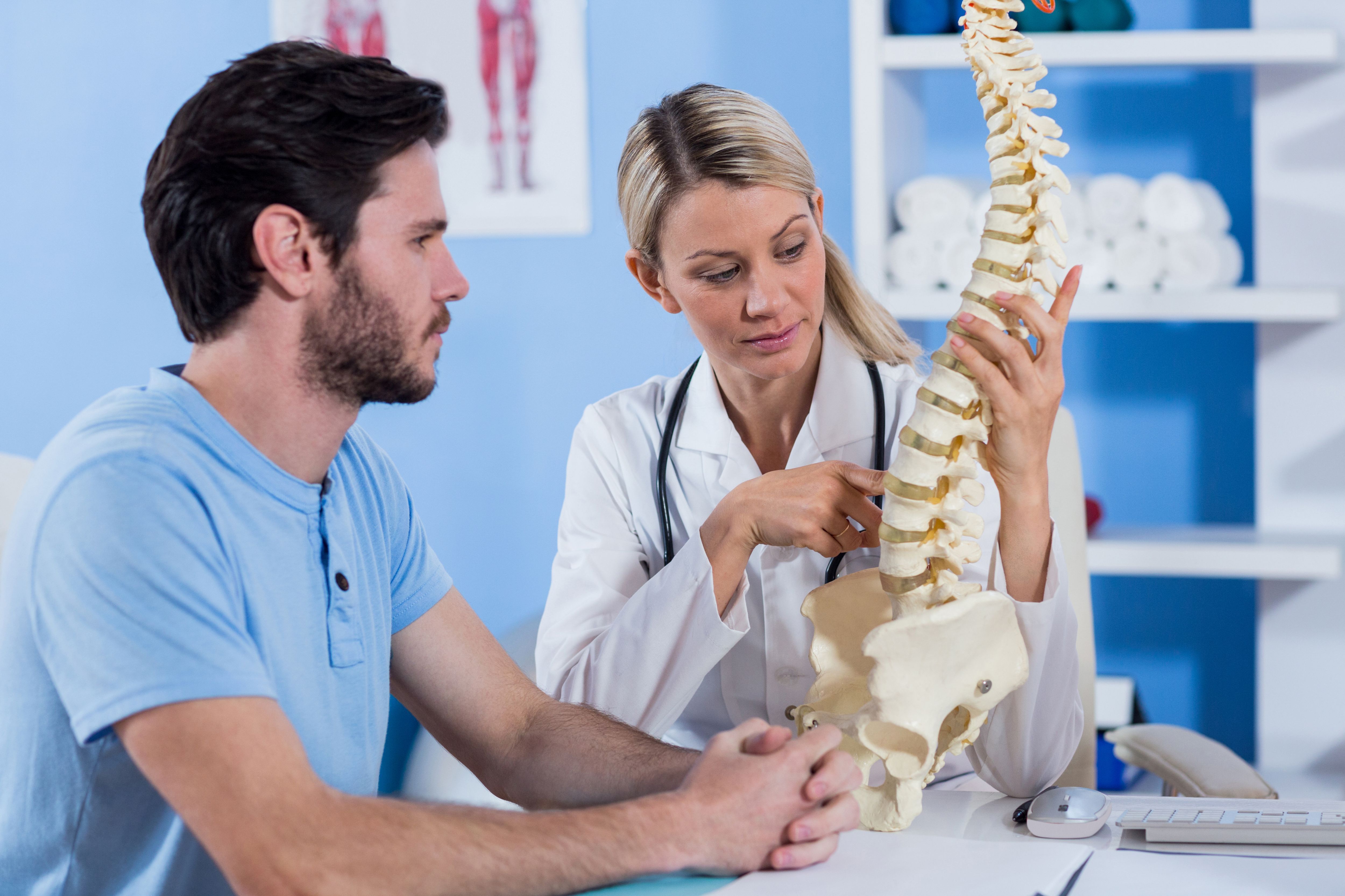 Ärztin zeigt einem Patienten ein Wirbelsäulenmodell